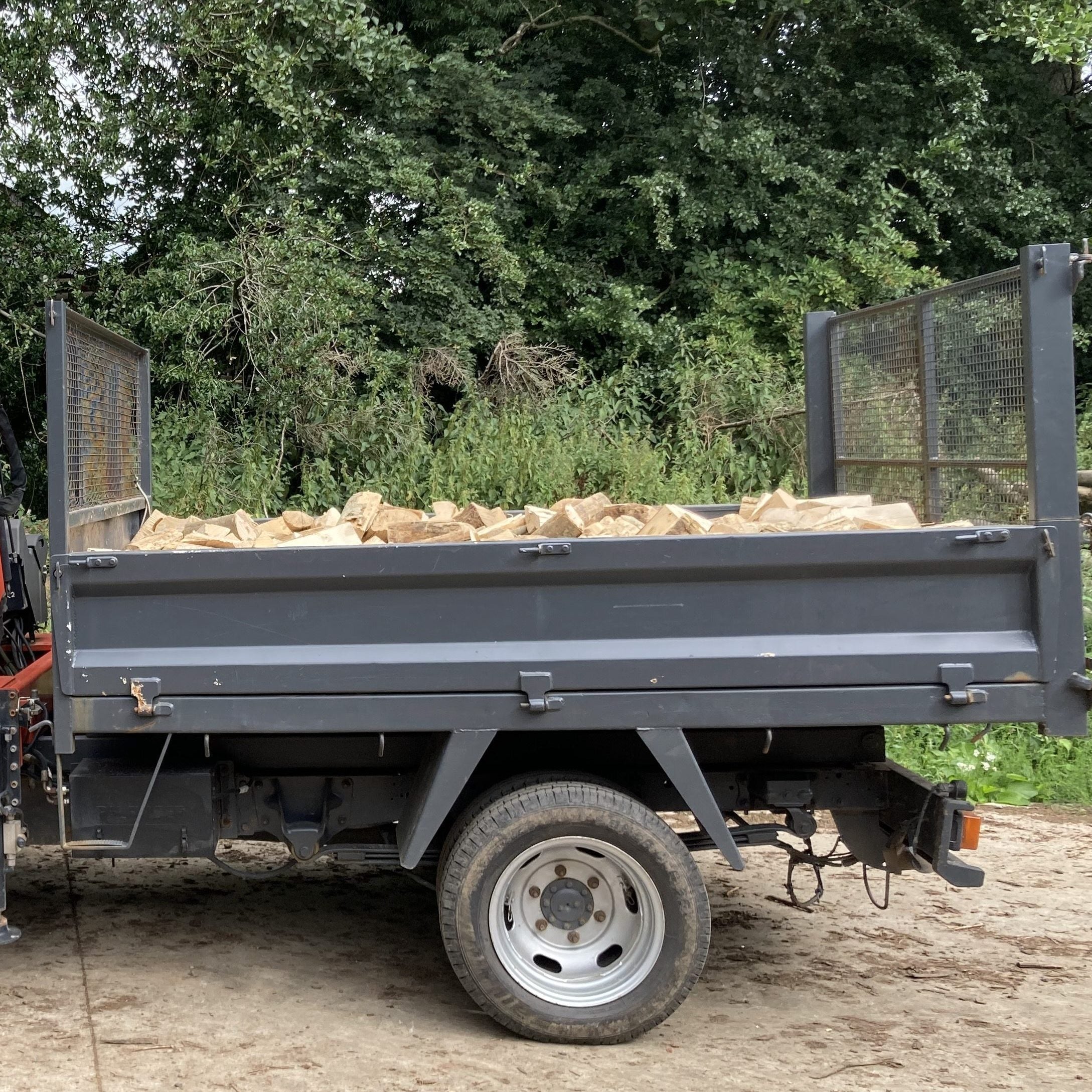 White truck with a crane and trailer loaded with kiln dried firewood logs in shropshire, surrounded by greenery.